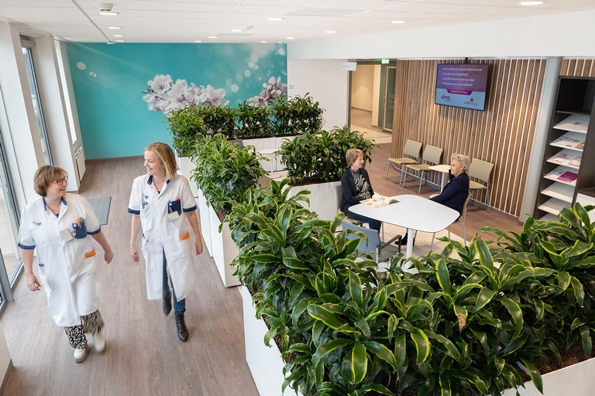 Twee verpleegkundigen lopen langs wachtruimte Oncologisch Centrum Twee verpleegkundigen lopen langs wachtruimte Oncologisch Centrum